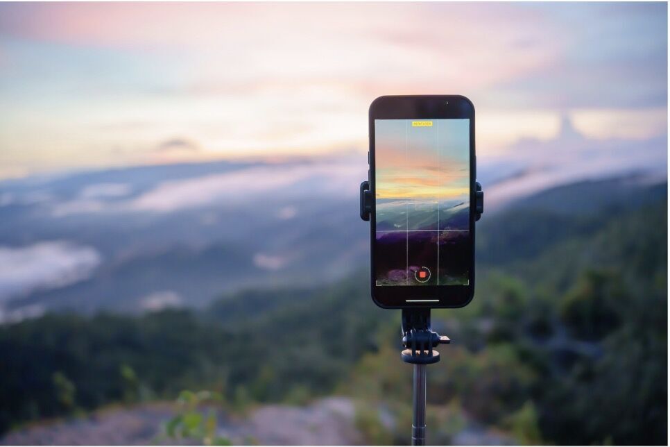 Deux mains tiennent un smartphone filmant un coucher de soleil